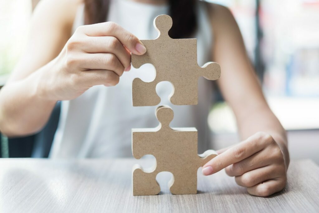 Woman hands connecting couple puzzle over table, businessman holding wood jigsaw inside office